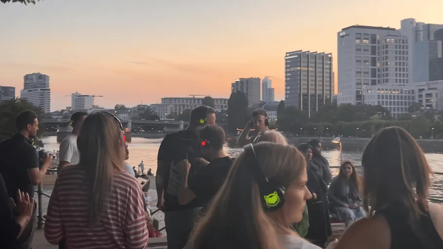 People wearing headphones at riverside sunset gathering.