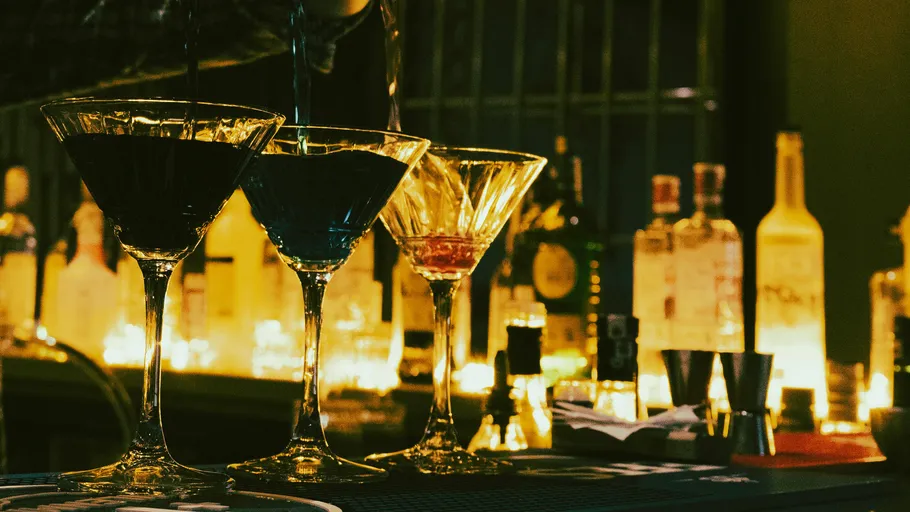 Martini glasses being filled on a dimly lit bar.