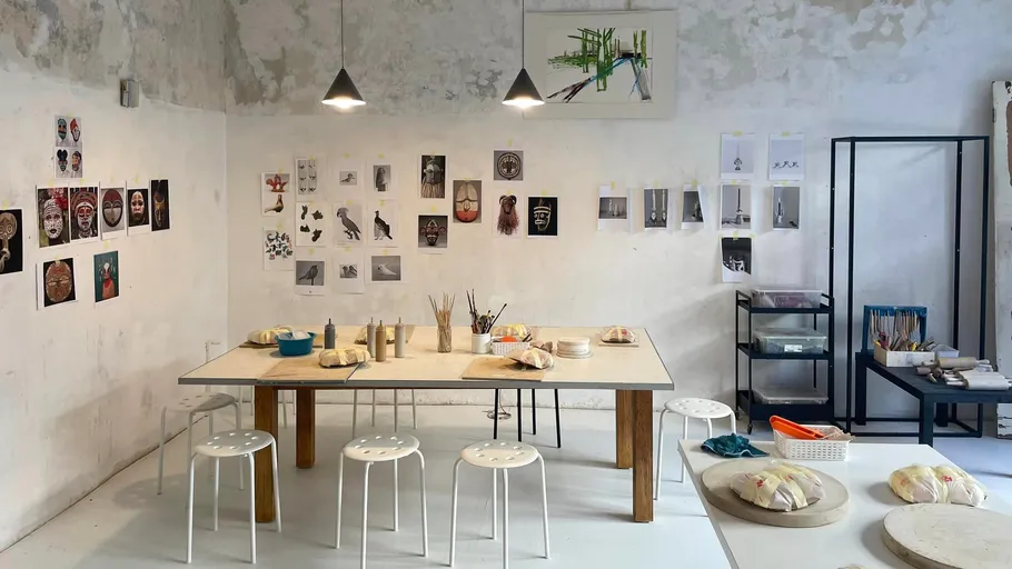 Kunststudio mit Tisch, Hockern und Wandkunst.