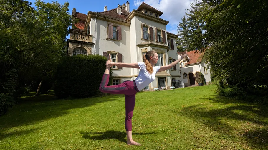 Woman doing yoga pose in garden with large house.