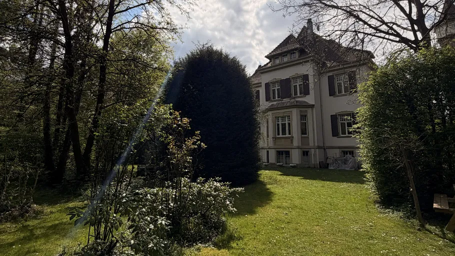Großes Haus mit Garten unter wolkigem Himmel.
