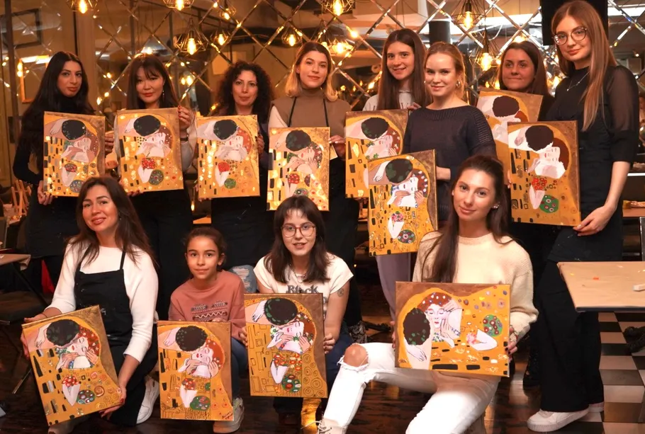 Group posing with paintings in brightly lit room.