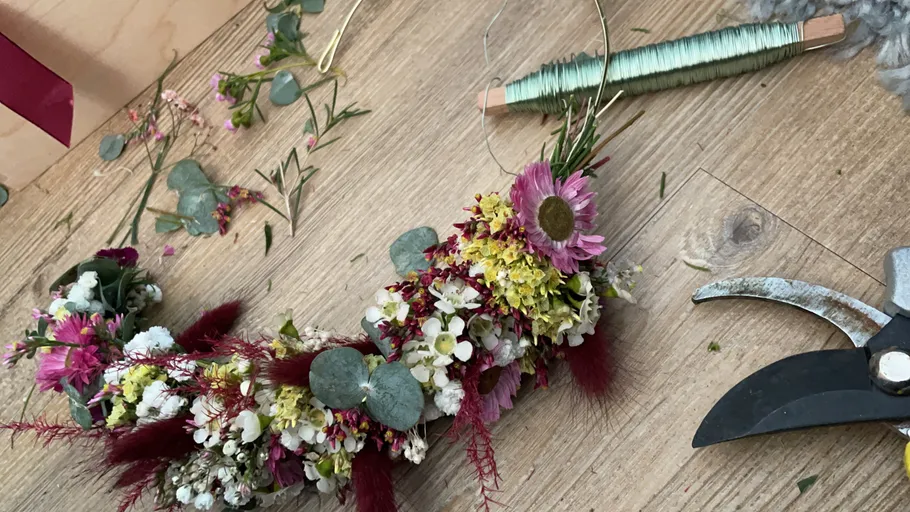 Floral wreath being crafted on wooden surface.