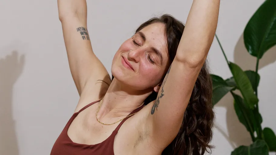 Woman stretching with arms raised, smiling indoors.