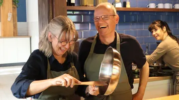 Zwei Personen kochen und lachen in einer Küche.