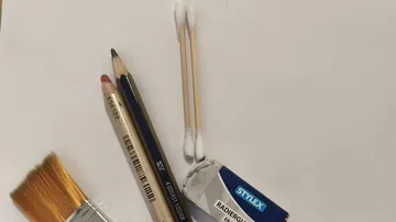 Bleistifte, Stäbchen, Radiergummi, Pinsel auf weißem Papier.