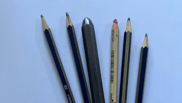Five pencils and one metal stylus on paper.