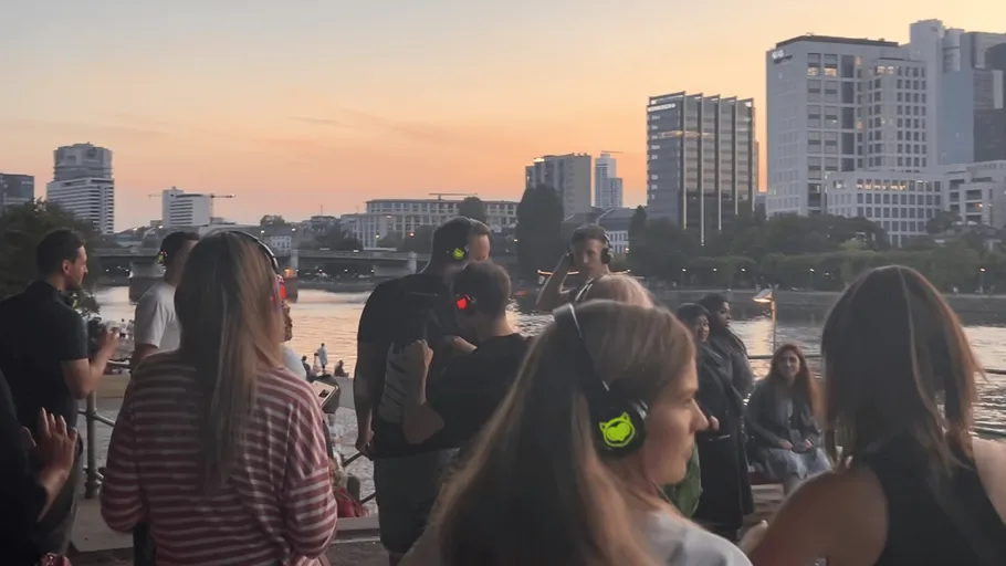People with headphones dancing by river at sunset.