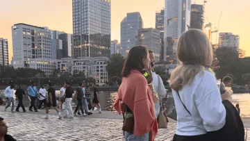 People walking by river in city at sunset.