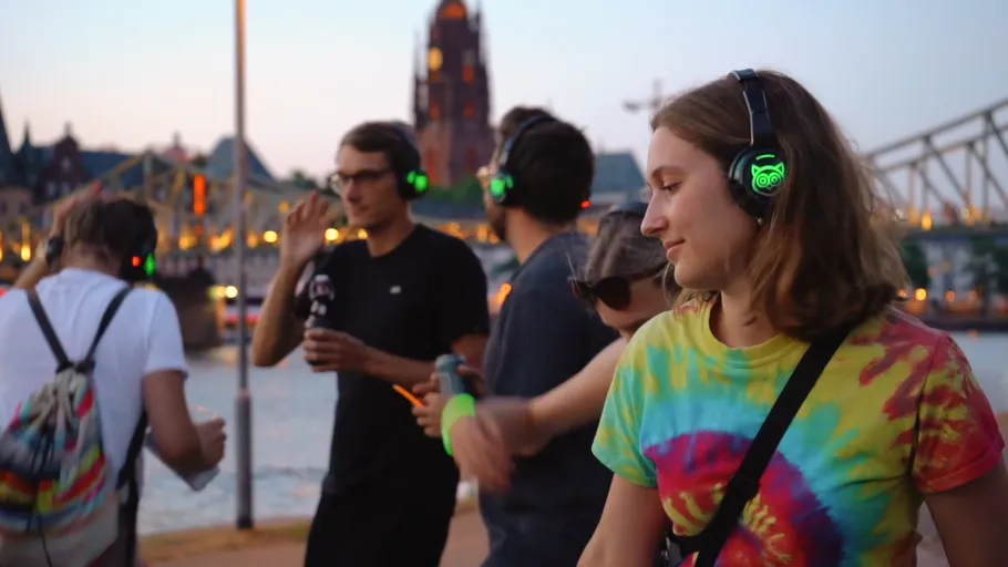 People wearing headphones dancing outdoors near river.