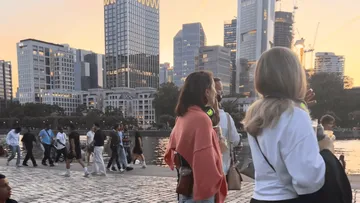 Menschen gehen am Wasser, Skyline im Hintergrund.