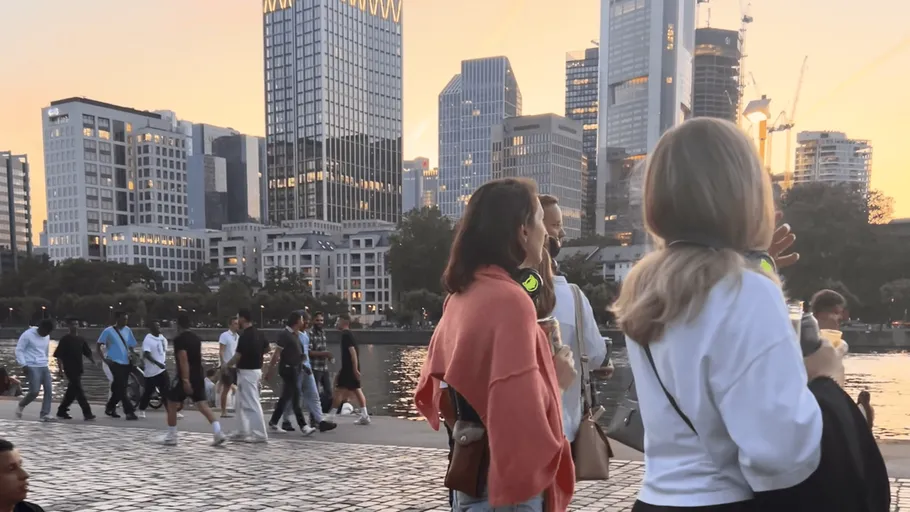 Menschen gehen am Wasser, Skyline im Hintergrund.
