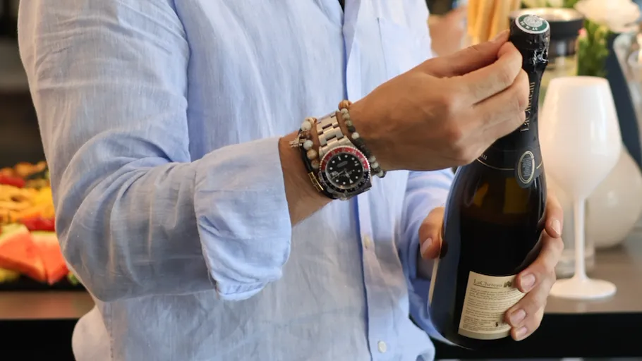 Person öffnet Weinflasche drinnen, trägt Uhr.