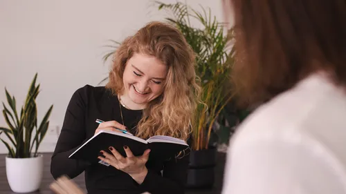 Woman writing in notebook, smiling, indoor plants.