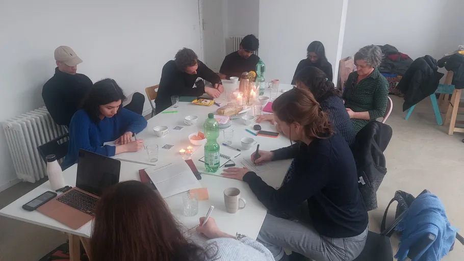 Personen schreiben an einem Tisch in hellem Raum.