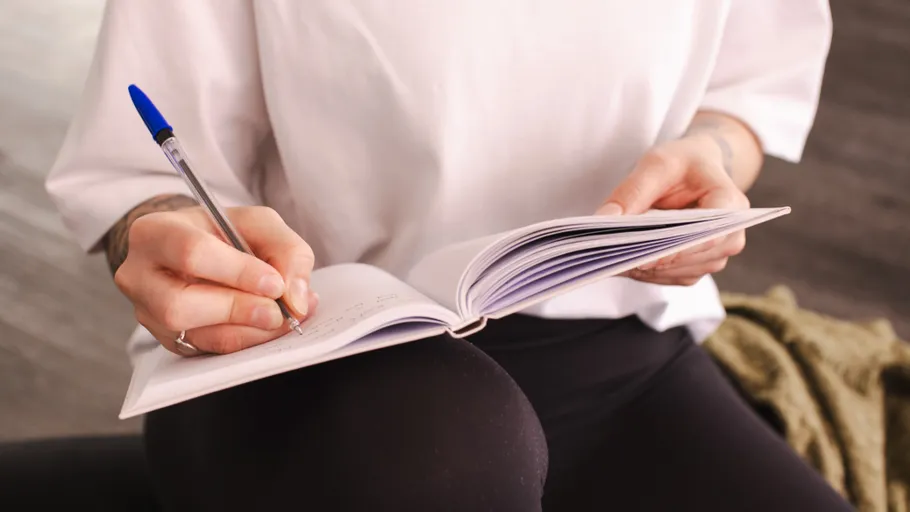 Person writing in notebook, sitting indoors.