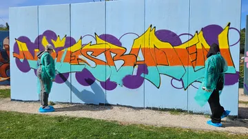 Zwei Personen malen bunte Graffiti an Wand.