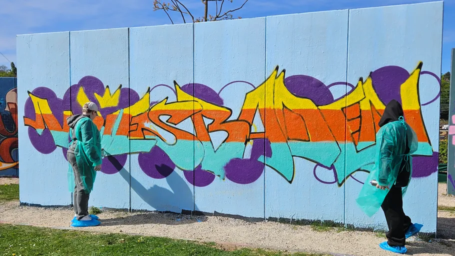 Zwei Personen sprühen Graffiti an eine Wand.