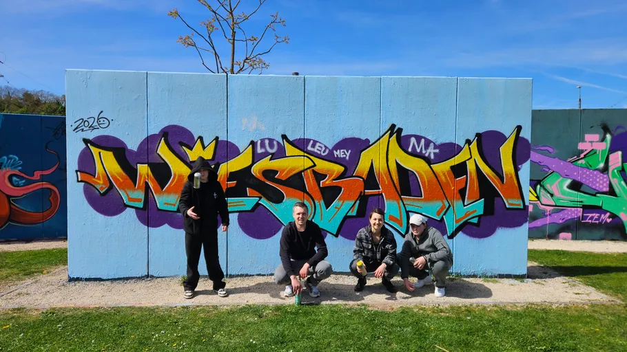 Vier Personen mit Graffiti-Wand draußen.
