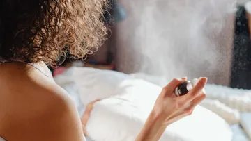 Woman sprays mist on bed in bedroom.