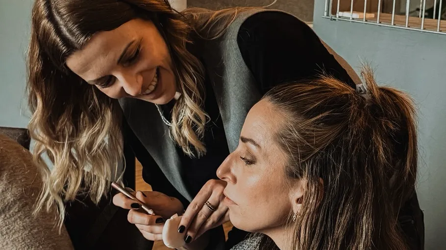 Zwei Frauen lächeln, eine hält Handy drinnen.