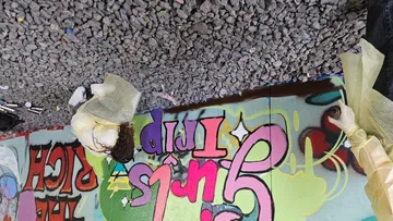 Personen malen buntes Graffiti unter Brücke.