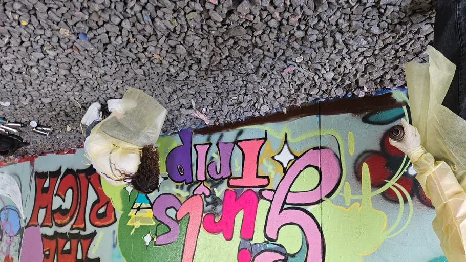 Personen malen buntes Graffiti unter Brücke.
