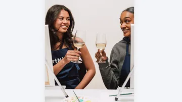 Two women clinking wine glasses at table.