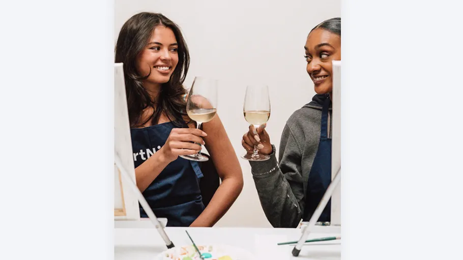 Zwei Frauen stoßen mit Weingläsern an Tisch an.