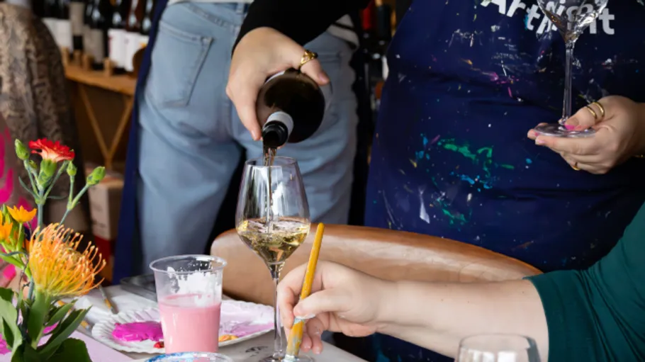 Person schenkt Wein ein, während jemand malt drinnen.