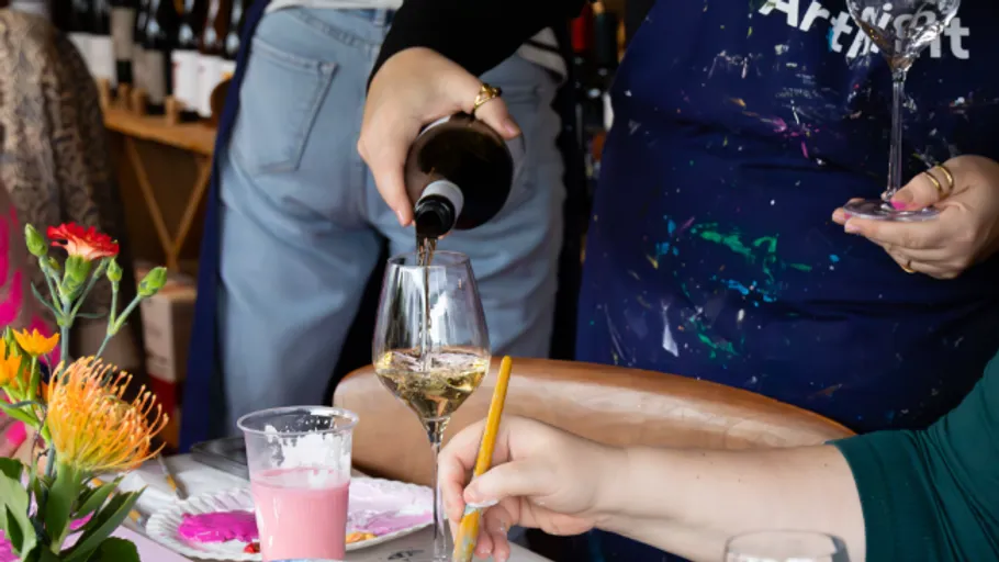 Person pours wine into a glass at a table.