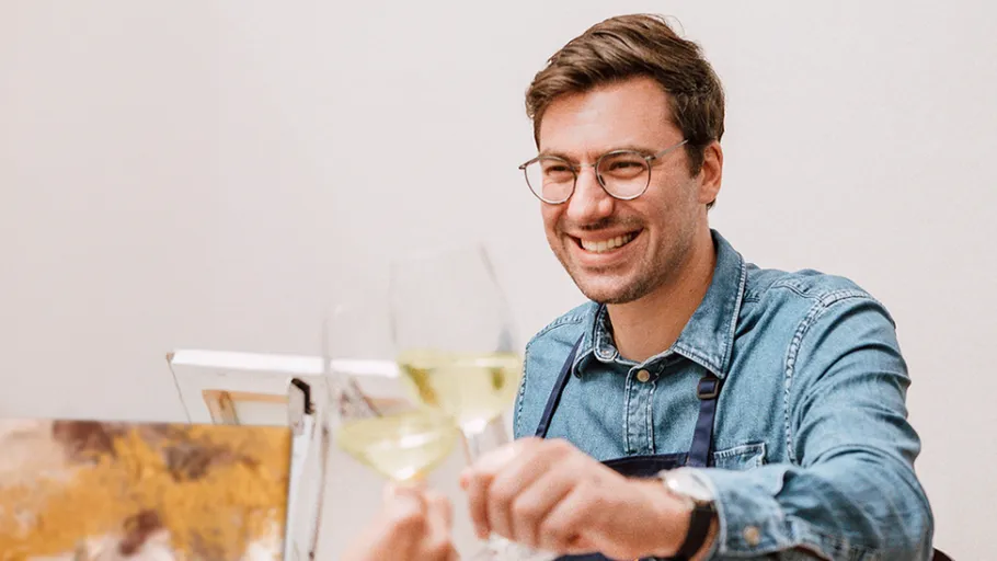 Mann mit Brille stößt mit Wein an drinnen.