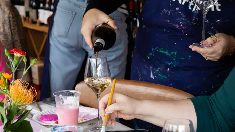 Person schenkt Wein bei einem Malkurs ein.