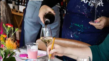 Person schenkt Wein bei Kunstveranstaltung ein.
