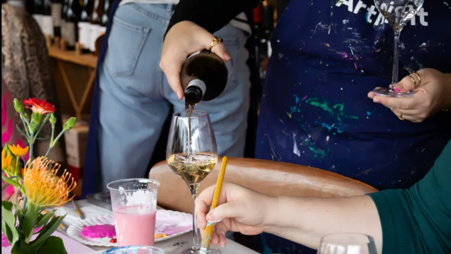 Person schenkt Wein bei Kunstveranstaltung ein.