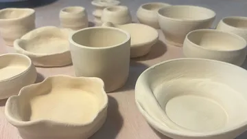 Unglasierte Tontöpfe und Becher auf Holztisch.