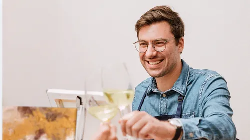 Mann lächelt, stößt Gläser an, drinnen.