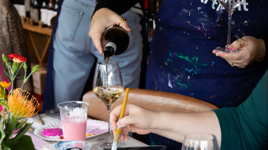 Person schenkt Wein ein, während andere malt.