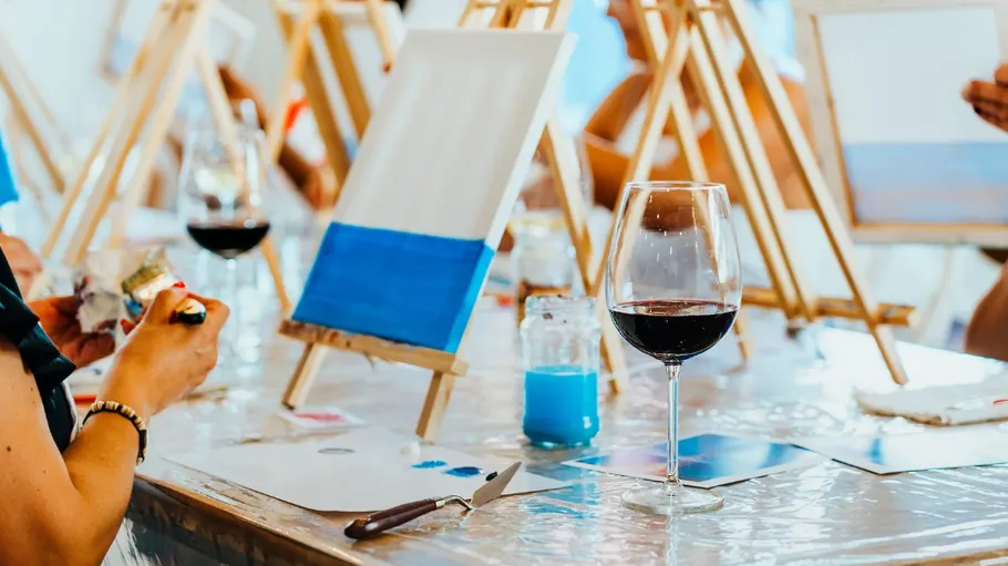 People painting on easels, glass of wine present.