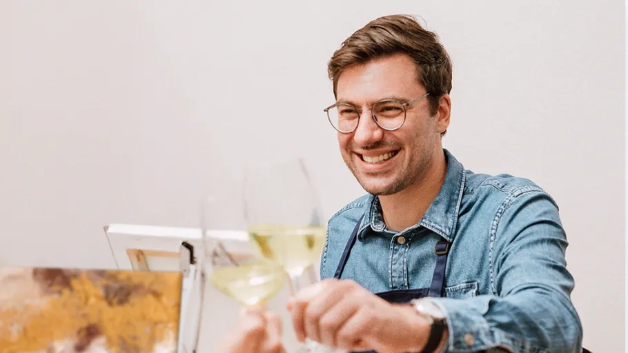 Lächelnder Mann stößt mit Weingläsern drinnen an.