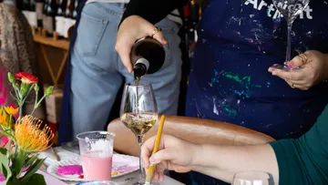 Person gießt Wein während eines Kunstkurses ein.
