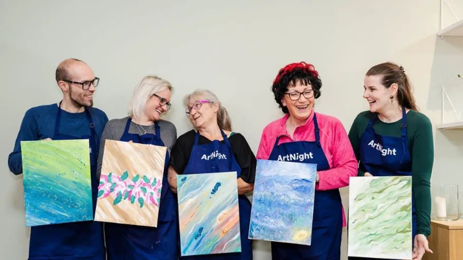 Five people smiling, holding paintings in studio.
