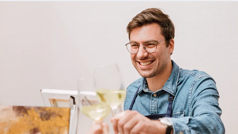 Lächelnder Mann stößt mit Weißwein drinnen an.