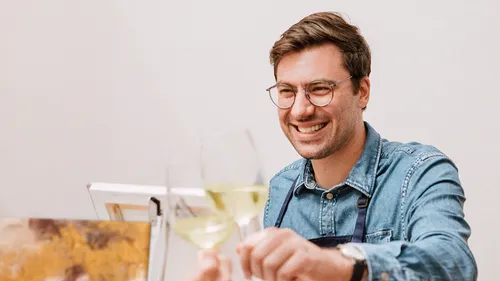 Lächelnder Mann stößt mit Weißweingläsern an.
