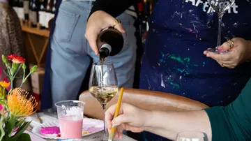 Wine pouring at art event, colorful table.