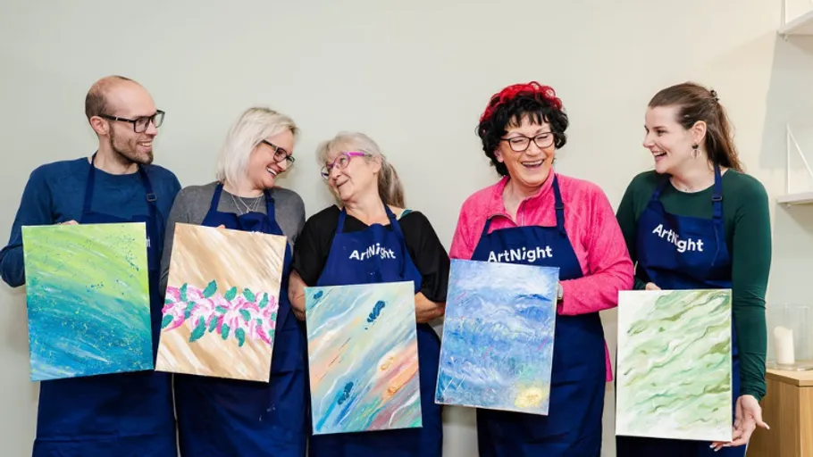 Five people holding abstract paintings, smiling indoors.