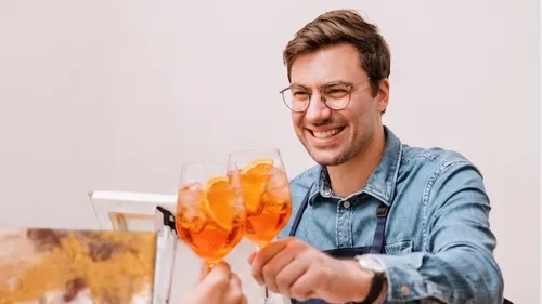 Mann lächelt beim Anstoßen mit orangefarbenen Getränken.