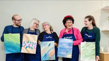 Five people smiling while holding their paintings.