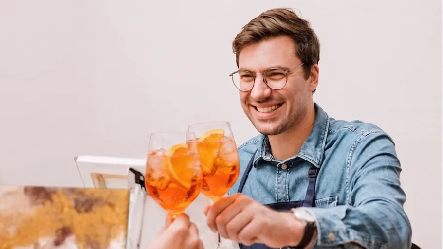Mann stößt mit Getränken an, lächelt drinnen.