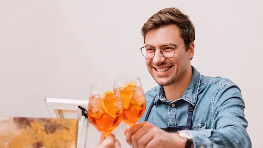Mann lächelnd, stößt mit orangefarbenen Getränken an.